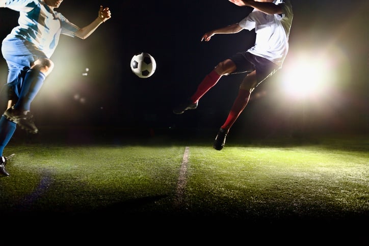 Athlete jumping towards soccer ball on field during game.